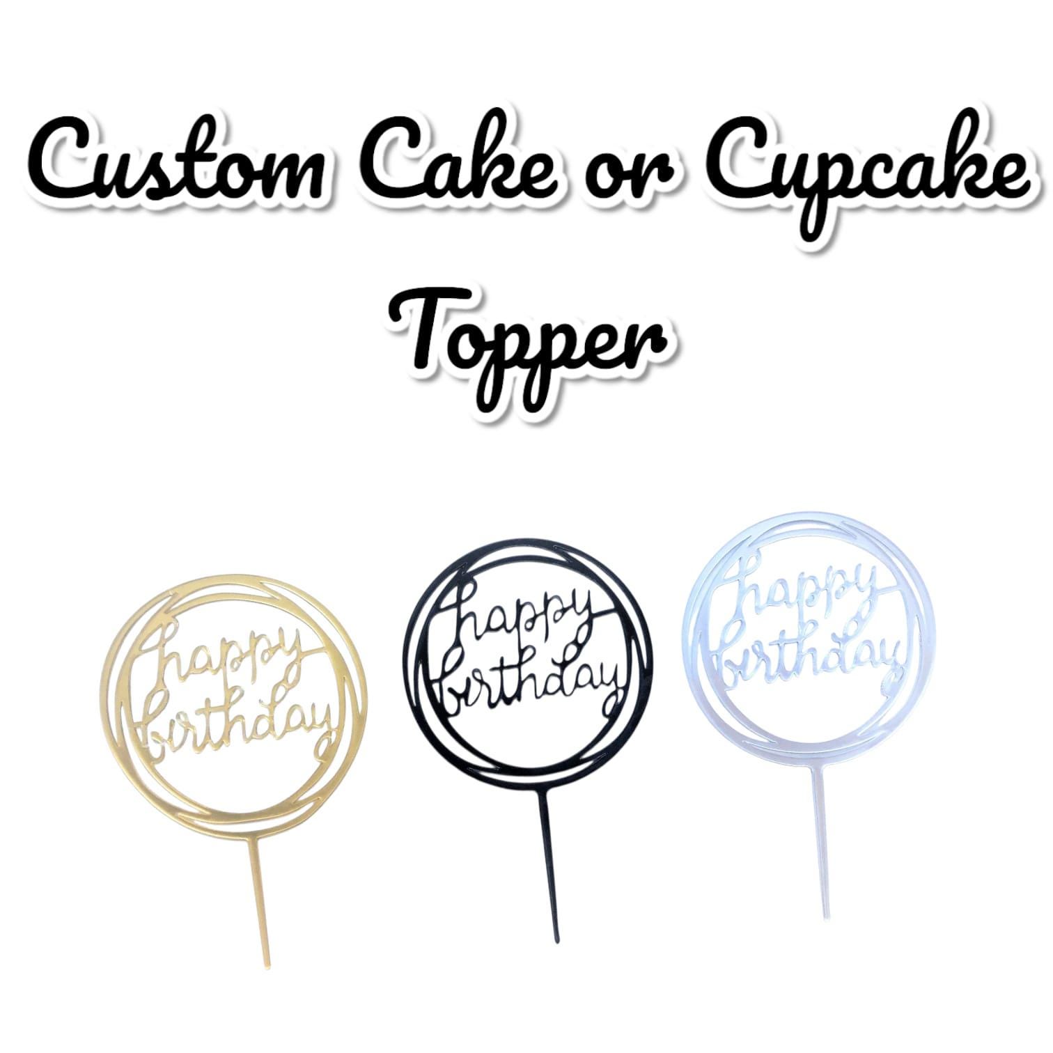 Three cake toppers with the words "Happy Birthday" in a circular design. One is gold, one is black, and one is silver. The text "Custom Cake or Cupcake Topper" is above the toppers.
