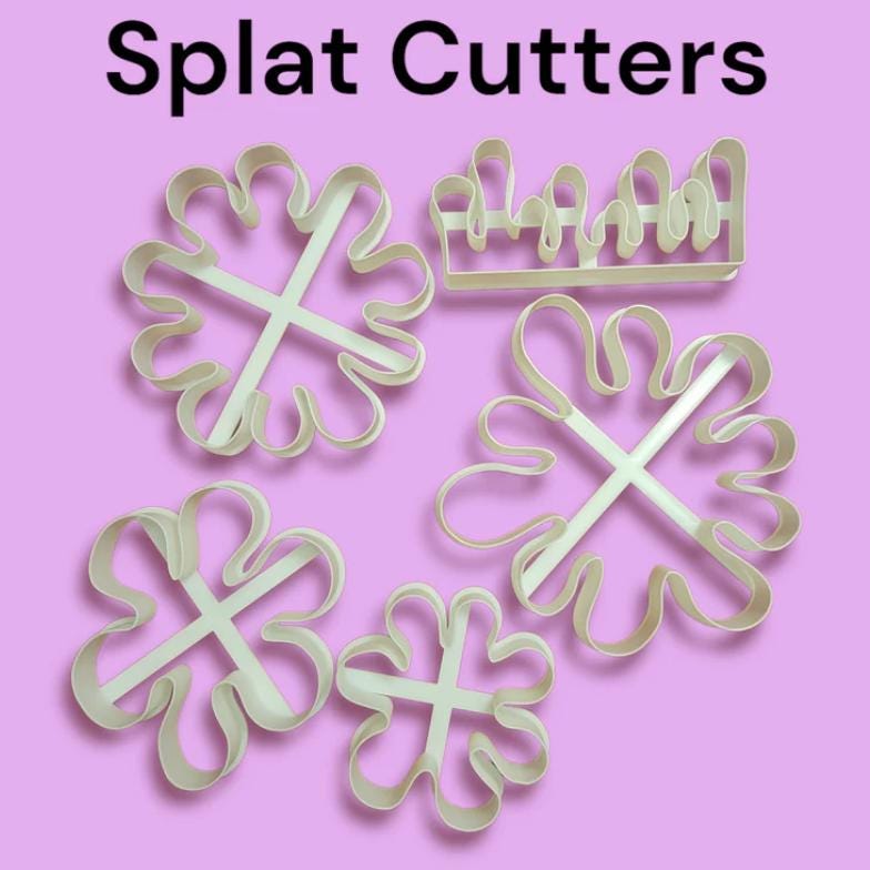 A collection of white plastic splat-shaped cookie cutters and a crown-shaped cutter on a light purple background. The text "Splat Cutters" is at the top of the image.