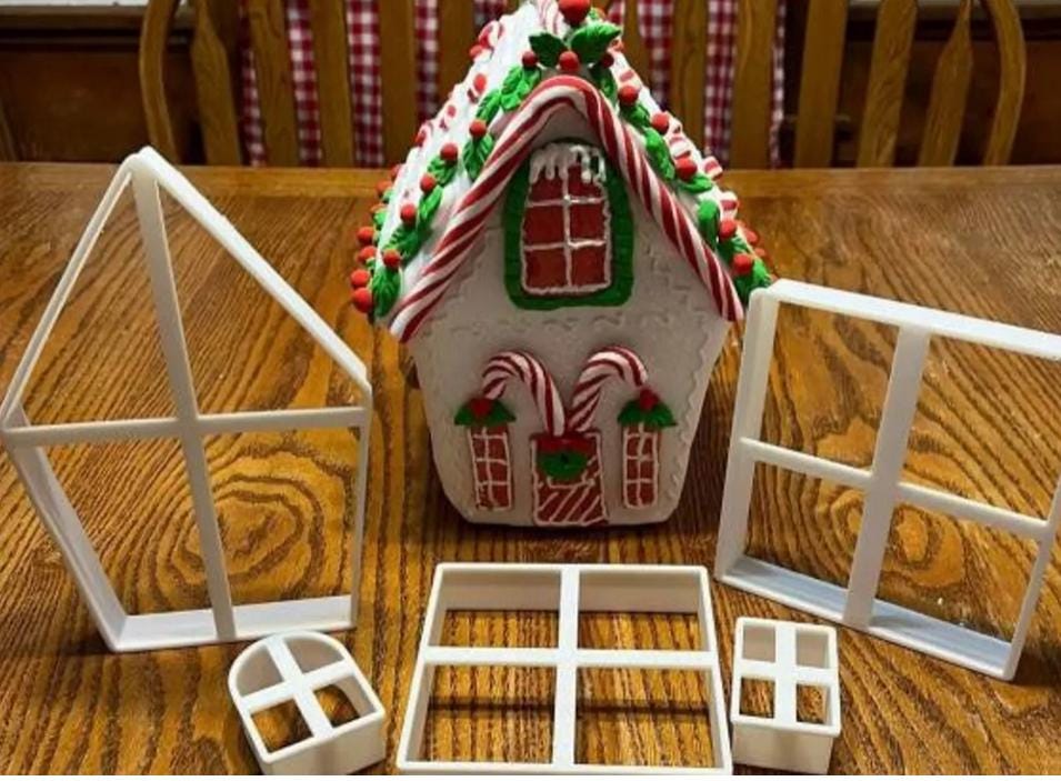 A decorated gingerbread house with candy cane accents and a red and green roof, surrounded by white plastic window frame molds. The house features candy cane details and a festive holiday theme.