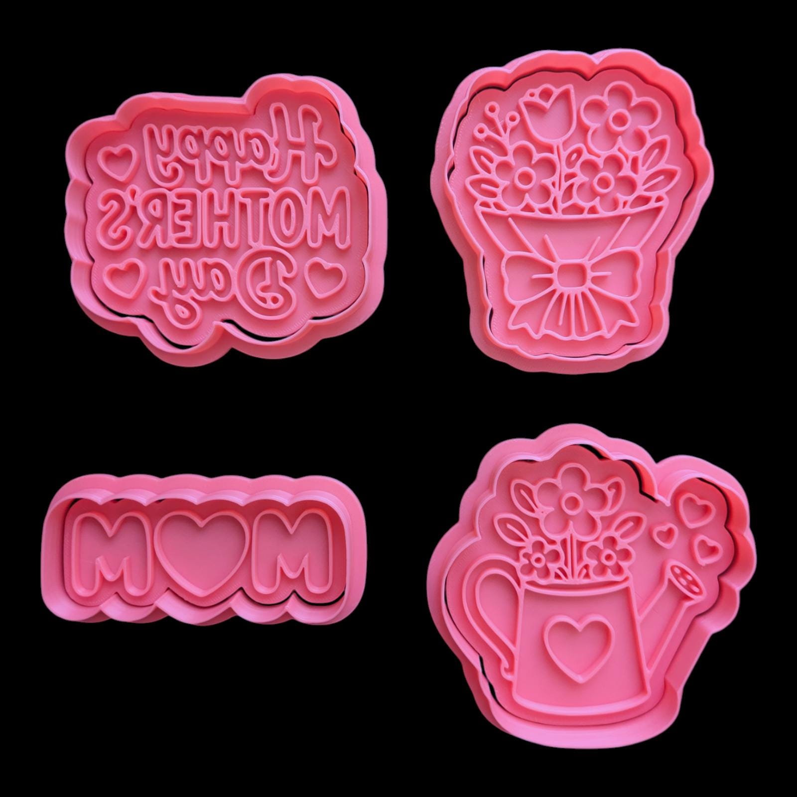 Four pink cookie cutters on a black background. The cutters include a "Happy Mother's Day" design, a bouquet of flowers, the word "MOM" with a heart, and a watering can with flowers and hearts.
