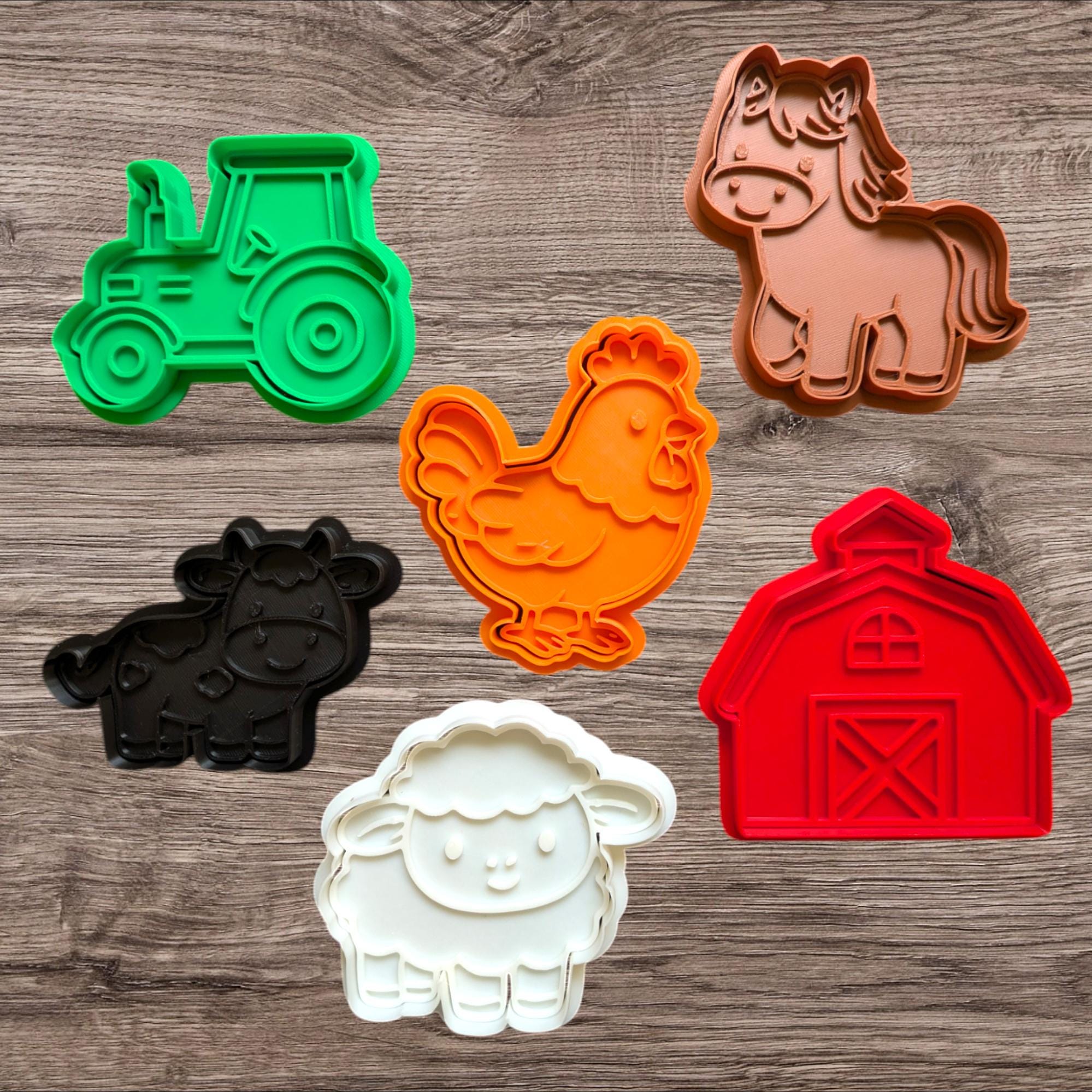 A collection of colorful farm animal and object cookie cutters. Includes a green tractor, a brown horse, an orange chicken, a black cow, a white sheep, and a red barn. These are ideal for making farm-themed cookies.