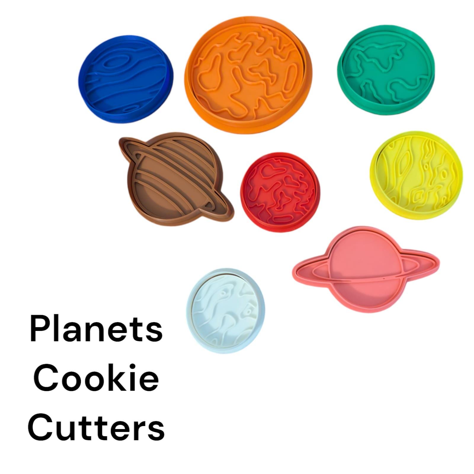 A collection of colorful planet-shaped cookie cutters. The cutters are in various colors, including blue, orange, green, brown, red, yellow, light blue, and pink. The text "Planets Cookie Cutters" is displayed in black.